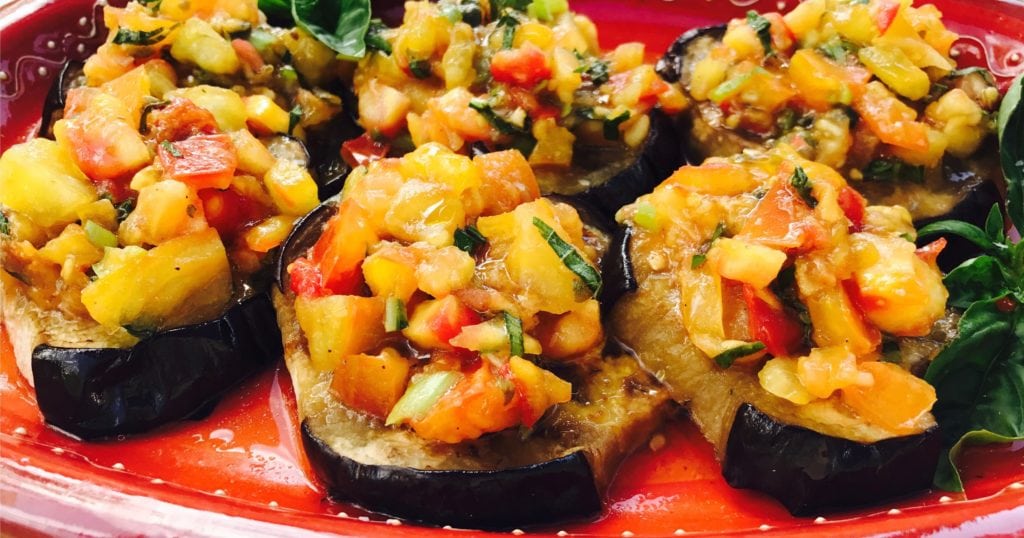 Baked eggplant discs topped with tomato salsa on red platter