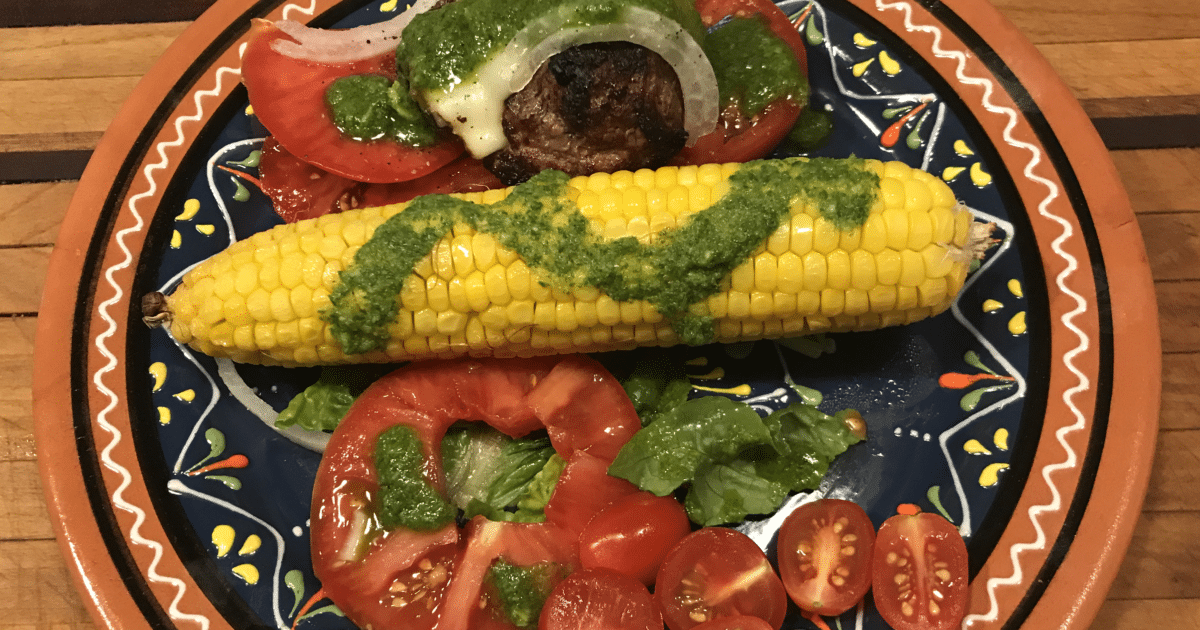 Green sauce, Mojo de Perejil, poured on top of corn on the cob, tomato salad and meat